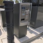 Black 6-inch Metro Decorative Bollard Covers used to protect a parking lot gate kiosk
