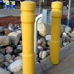 Yellow 6-inch Architectural Decorative Bollard Covers used to guard an entry gate's knock box